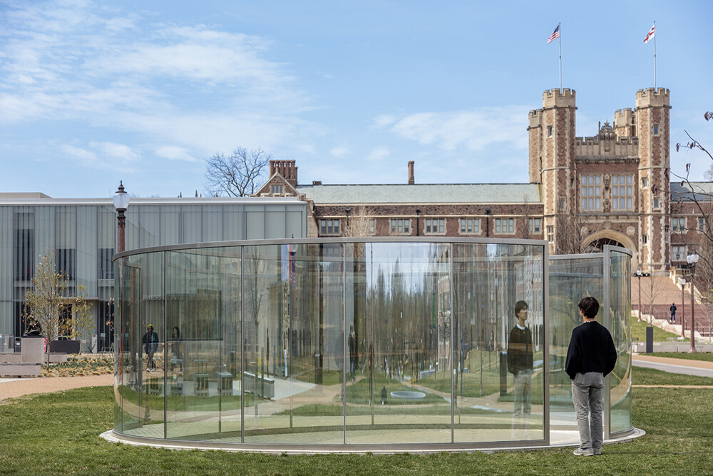 An outdoor sculpture that is circular and reflective. A person is standing looking at their reflection in the sculpture.