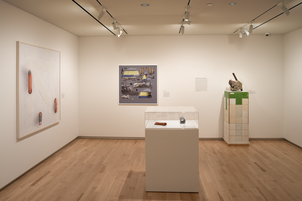 Installation view of a gallery: two artworks on the walls, two objects in a standing display case, and one standing sculpture