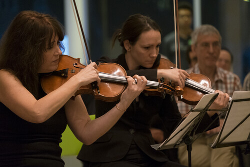 Two people playing violin as another person looks on