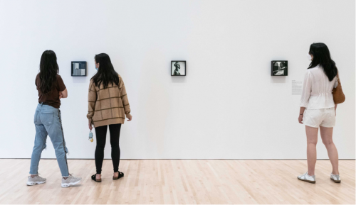 Three people observe a row of three framed black-and-white compositions on a wall.