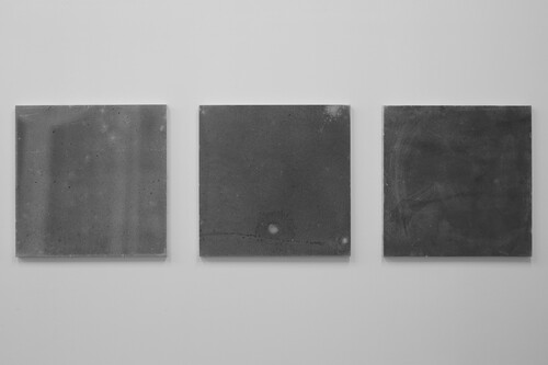 Four square, gray canvases on a wall, getting progressively darker from left to right