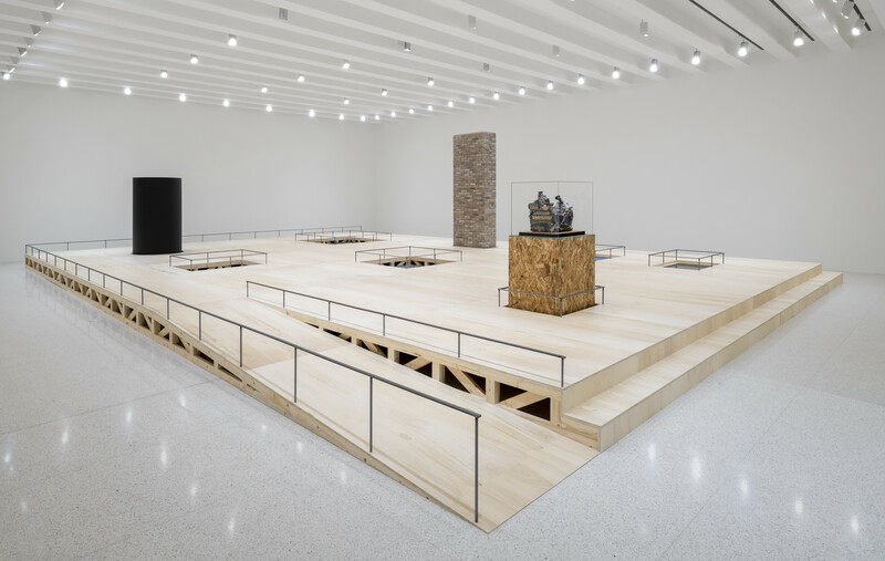 Installation view of a wooden platform with a ramp, with various sculptures placed throughout