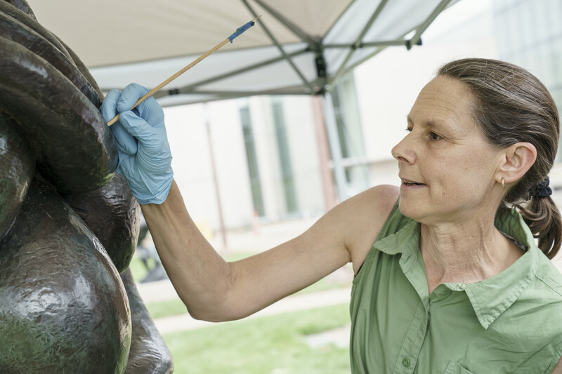 A person doing conservation work on a sculpture outside. 